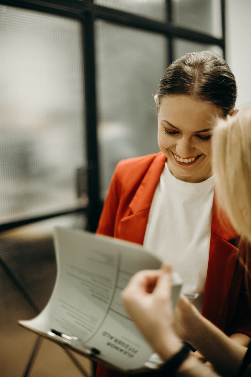 Two young women discussing documents in a modern office environment, smiling and engaged.